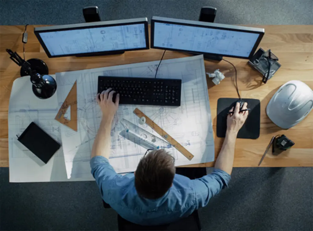 An overhead photo of a worker at a desk with keyboard, mouse and two screens